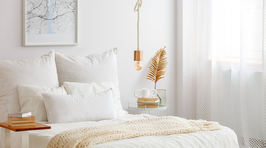 Close up of white and airy bedroom focusing on bed with white bedding and bedside tables on each side of the bed with books on them